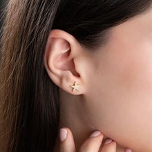 Close-up of an ear wearing a gold star-shaped earring with a blurred background