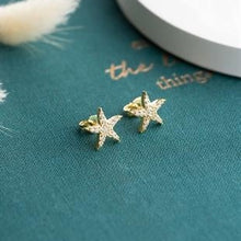 Star-shaped earrings on a teal surface with decorative text