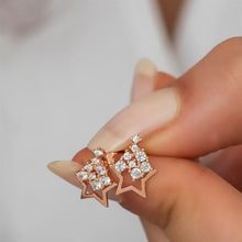 Rose gold star-shaped earrings with clear gemstones held between fingers against a neutral background