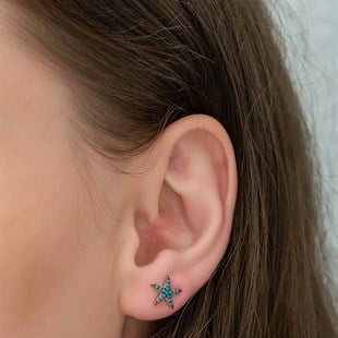 Close-up of an ear with a star-shaped blue earring against a neutral background