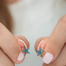 Turquoise starfish earrings held between fingers against a neutral background