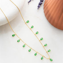 Gold necklace with green gemstones on a white surface