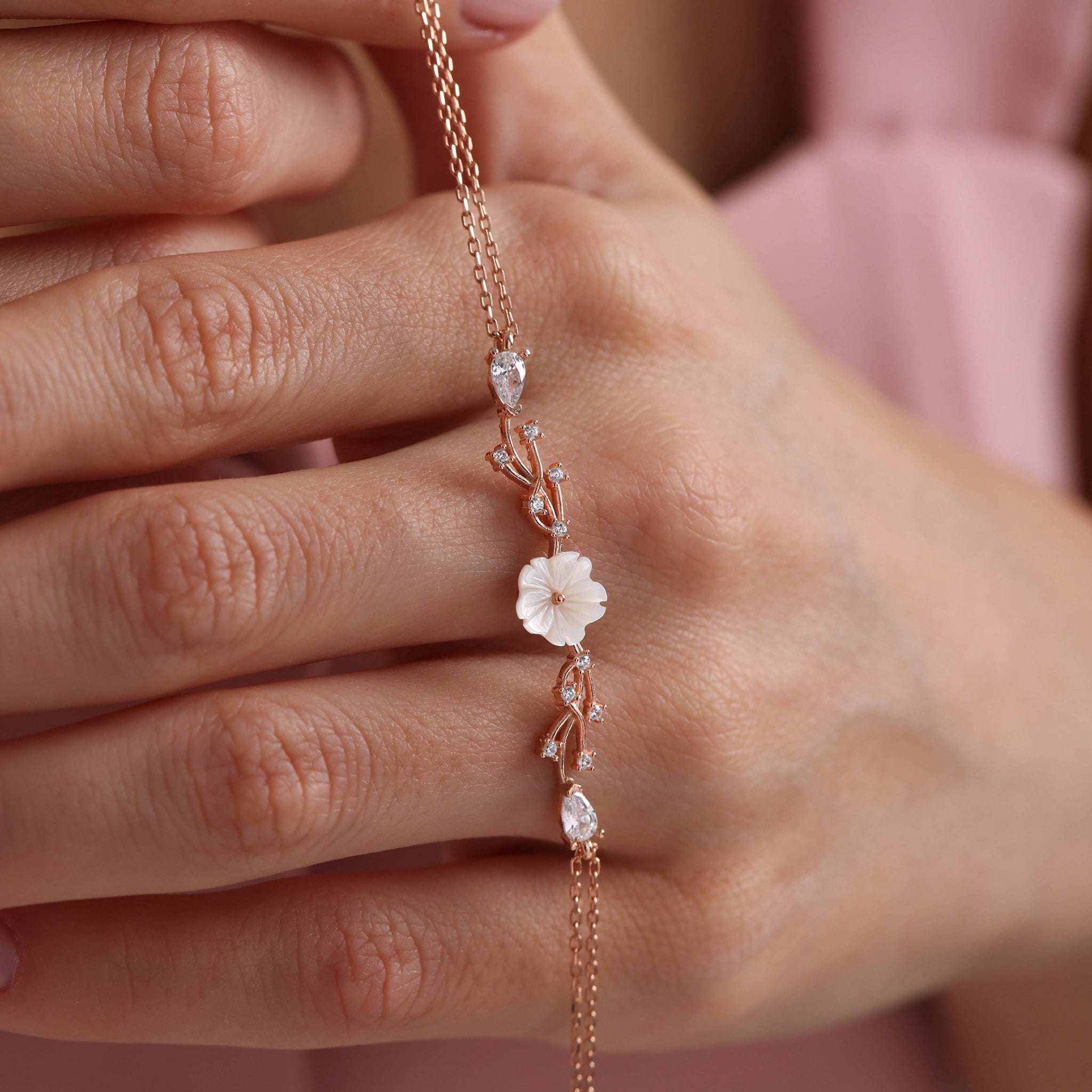 Rose gold bracelet with floral design on a hand against a blurred background