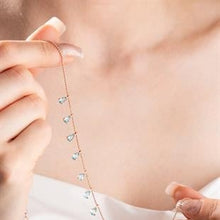 Close-up of a delicate necklace with small heart pendants being held near a person's neck.
