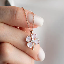 Rose gold necklace with a delicate pink flower pendant held by a hand against a blurred background