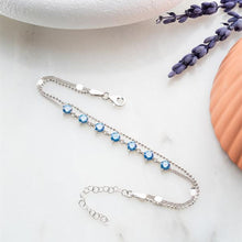 Silver necklace with blue beads on a white surface with lavender flowers.