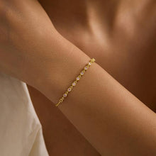 Gold bracelet with small stones on a wrist against a neutral background