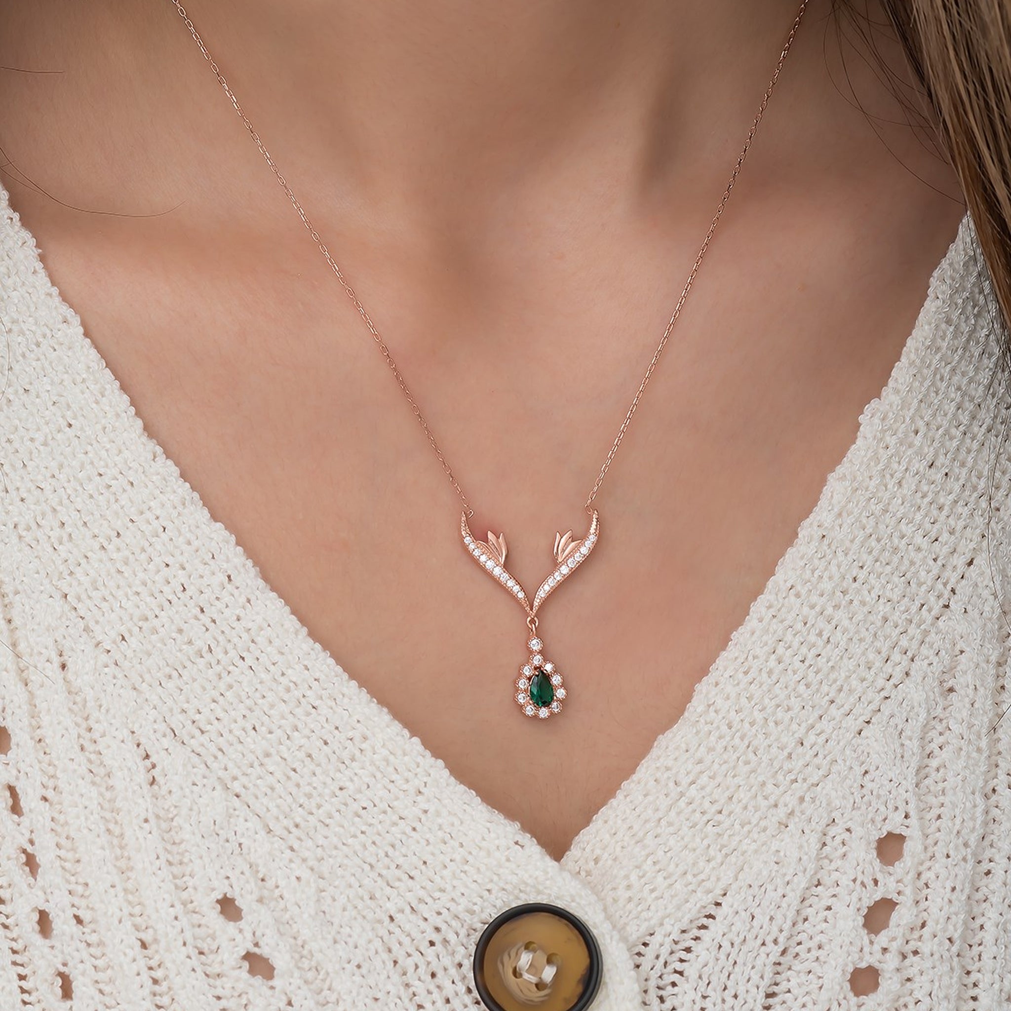 Rose gold necklace with a green gemstone pendant worn by a person in a white textured garment.