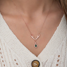 Rose gold necklace with a green gemstone pendant worn by a person in a white textured garment.