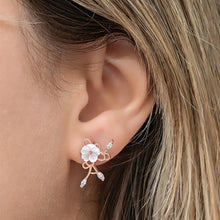 Close-up of an ear wearing a delicate floral earring with a blurred background