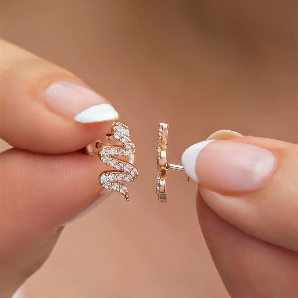 Rose gold earrings held between fingers against a neutral background