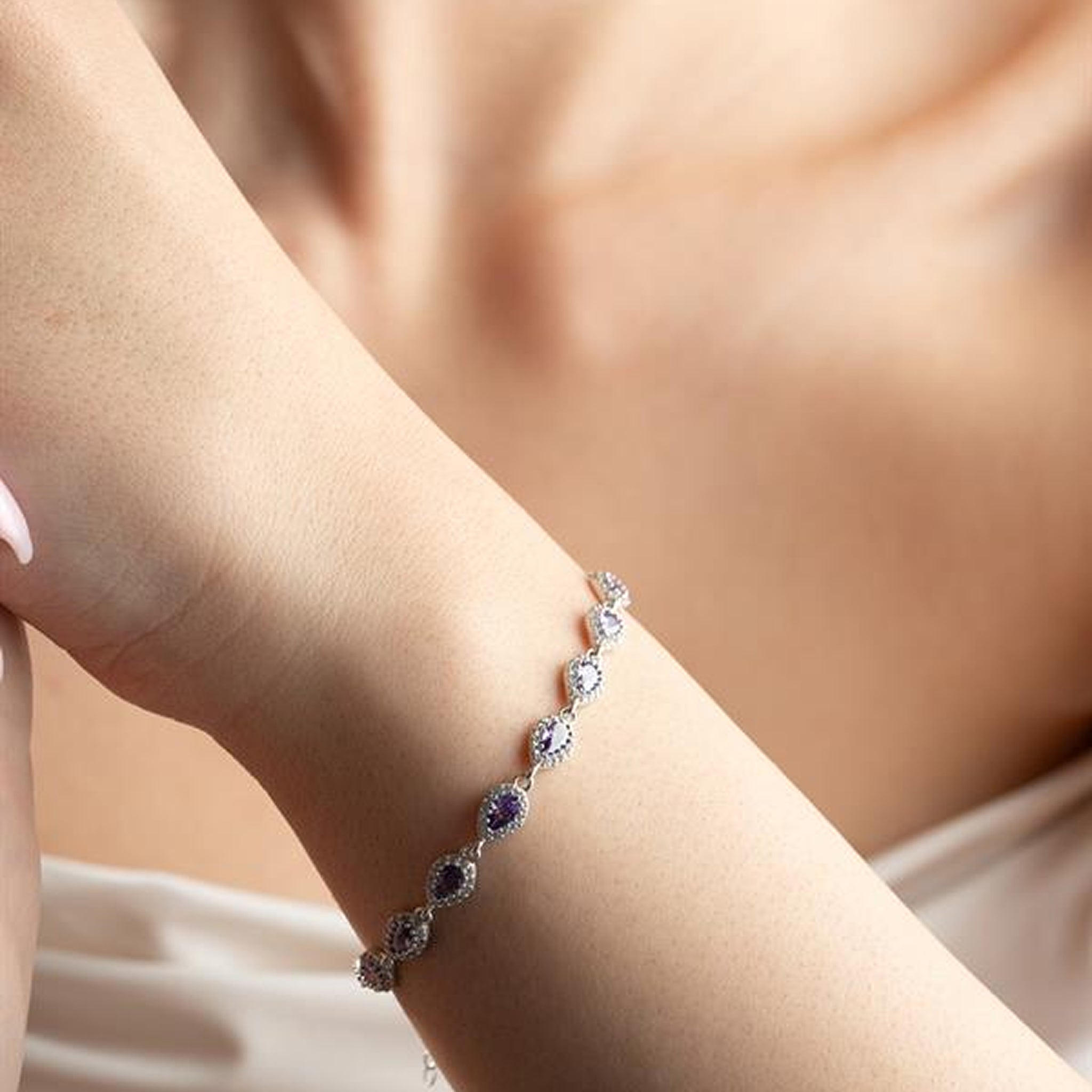 Silver bracelet with purple gemstones on a wrist against a neutral background