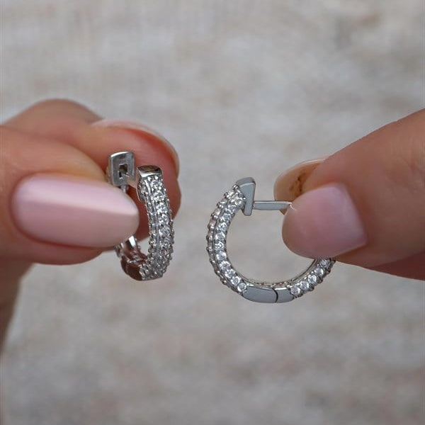 Silver hoop earrings held between fingers against a neutral background