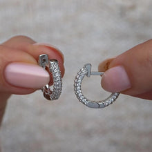 Silver hoop earrings held between fingers against a neutral background