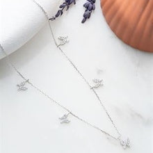 Silver necklace with small pendants on a white surface with lavender and a terracotta pot in the background.