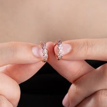 Rose gold hoop earrings being held between fingers against a neutral background