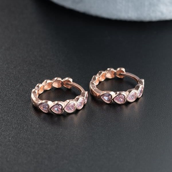 Rose gold hoop earrings with pink gemstones on a dark surface