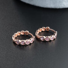 Rose gold hoop earrings with pink gemstones on a dark surface