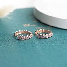 Two rose gold rings with pink gemstones on a teal surface.