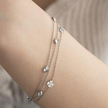 Multistrand bracelet with floral charms on a wrist against a neutral background