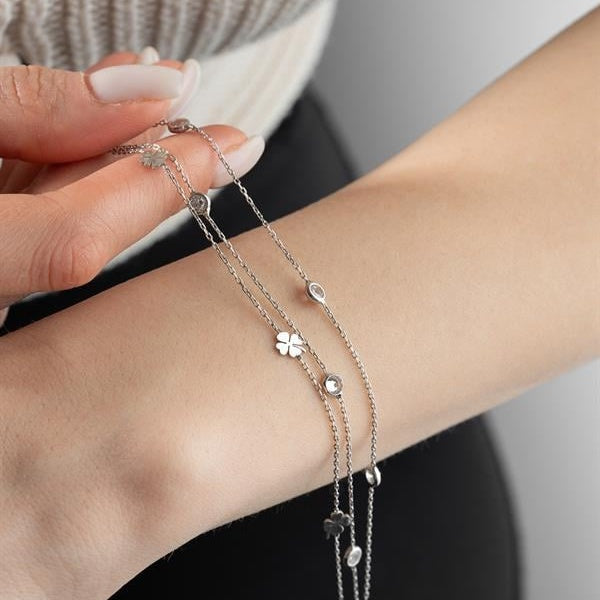 Close-up of a wrist wearing multiple silver bracelets with star and clover charms on a neutral background.