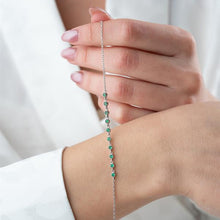 Close-up of a hand wearing a delicate bracelet with green beads on a plain background