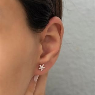 Close-up of an ear wearing a floral earring with a plain background