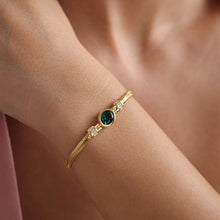 Gold bracelet with a green gemstone on a wrist against a neutral background