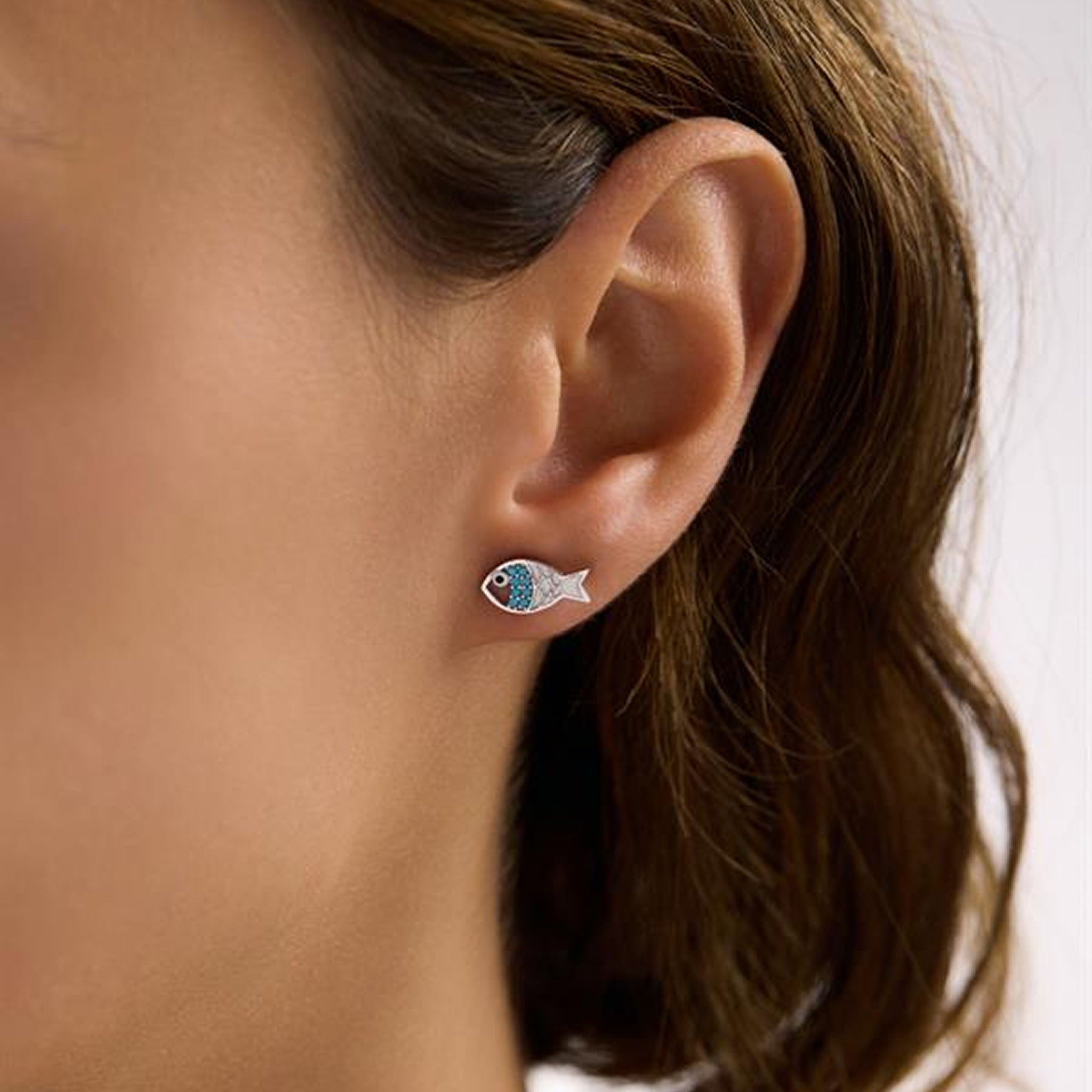 Close-up of an ear wearing a fish-shaped earring with a blurred background