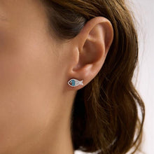 Close-up of an ear wearing a fish-shaped earring with a blurred background