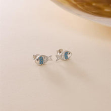 Silver fish-shaped earrings with blue stones on a beige background