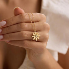 Gold flower-shaped necklace being held by a hand