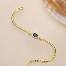 Gold bracelet with a blue gemstone on a beige background