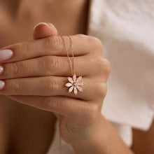 Hand holding a delicate necklace with a flower pendant against a neutral background