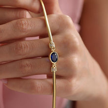 Gold bracelet with a blue gemstone worn on a wrist against a pink background