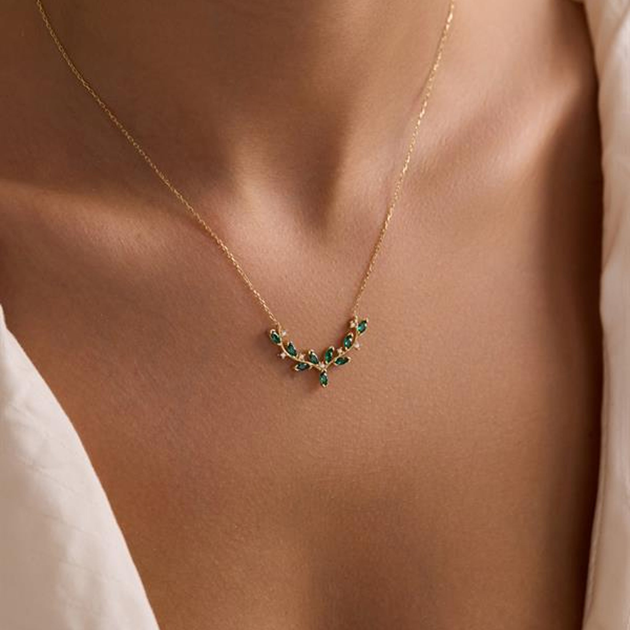 Gold necklace with green gemstones on a person wearing a white top.