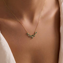 Gold necklace with green gemstones on a person wearing a white top.