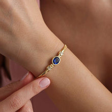 Gold bracelet with a blue gemstone on a wrist against a neutral background