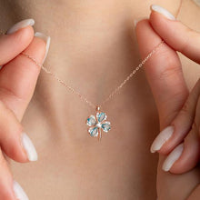 Rose gold necklace with a clover-shaped pendant held by hands against a neutral background