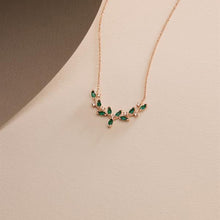 Rose gold necklace with green gemstones on a beige background