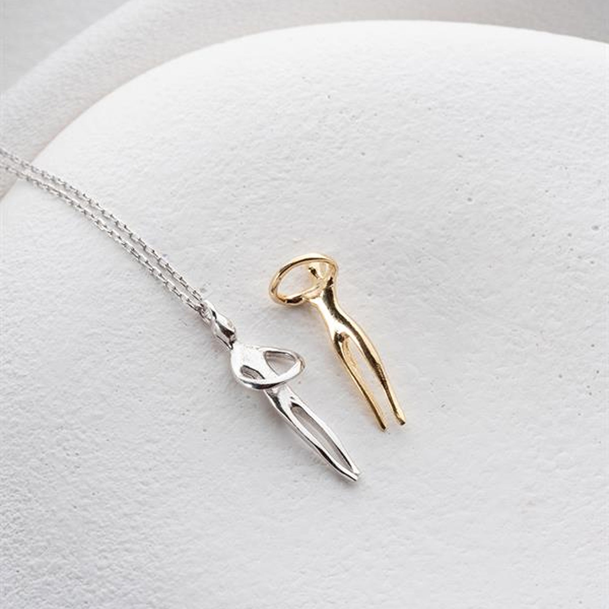 Two necklaces, one silver and one gold, on a light gray surface.
