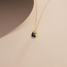 Gold necklace with a blue pendant on a beige background