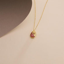 Gold necklace with a pink pendant on a beige background