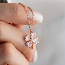 Rose gold necklace with a pink flower pendant held by a hand against a blurred background