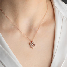 Rose gold necklace with a floral pendant on a person wearing a white shirt.