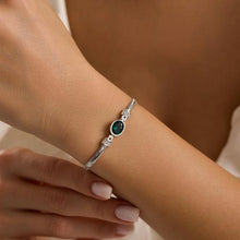 Silver bracelet with a green gemstone on a wrist against a neutral background