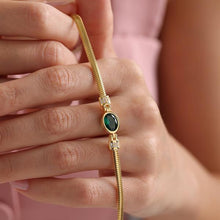 Gold bracelet with a green gemstone on a hand against a pink background