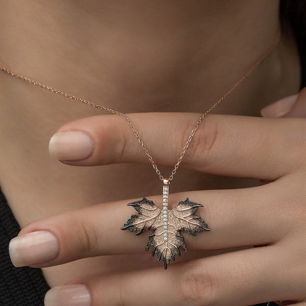 Necklace with a leaf pendant held by a hand against a neutral background