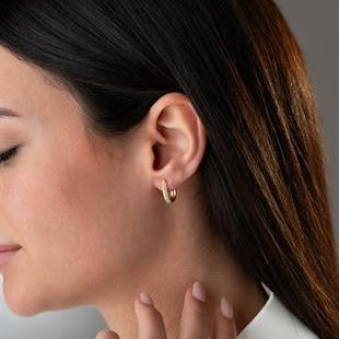 Close-up of a woman wearing a gold earring with a neutral background