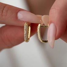 Gold hoop earrings held between fingers against a neutral background